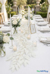 White artificial smilax willow leaf garland styled as a table runner on an elegant outdoor wedding reception table with candles and floral centerpieces