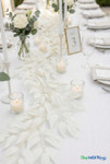 Close-up of white smilax leaf garland laid across a wedding reception table with glass votive candles and soft neutral place settings
