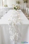 White artificial smilax willow leaf garland styled as a table runner on an elegant outdoor wedding reception table with candles and floral centerpieces