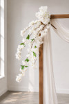 41" White Cascading "Spring Blossom" Spray – Extra-Full Silk Floral Waterfall from ShopWildThings.com attached to a simple wooden wedding arch in natural window light, with white fabric draping and white floral stems cascading downward.