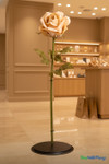Giant 42-inch Sand Silk Rose Bloom on display stand inside a modern retail showroom – large artificial statement flower from ShopWildThings used for luxury store or event décor.