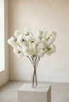 Artificial white cherry blossom branches in a clear glass vase, styled in a warm editorial studio setting for ShopWildThings.com