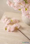 Close-up of light blush pink artificial cherry blossom branches with soft layered blooms and green leaves styled on a stone tabletop, ShopWildThings.com