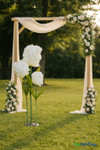 Large artificial white ivory tulip decor used as a floral prop at an outdoor wedding ceremony with wood arch and rose arrangements.