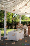 “Madrid” butterfly feather garland strands hanging as whimsical outdoor wedding or garden party backdrop, with floating orange and brown butterflies.