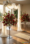 Artificial red rose trees displayed in indoor wedding ceremony aisle décor with white draping and romantic floral styling