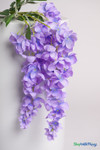 Close-up of lavender artificial wisteria cascading floral spray with realistic purple blossoms and green stems draped over a white studio pedestal from ShopWildThings.com