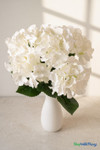 Artificial white hydrangea bouquet in matte white vase on clean stone surface with warm natural light for ShopWildThings.com