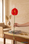 Real Feel Red Anthurium Tropical Stem, 27 inches tall, held by hand for scale in a warm resort-style interior, showing the long green stem and glossy red 6 inch bloom