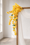 41" Yellow Cascading "Spring Blossom" Spray – Extra-Full Silk Floral Waterfall from ShopWildThings.com attached to a simple wooden wedding arch in natural window light, with white fabric draping and yellow floral stems cascading downward.
