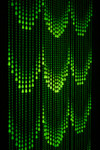 Alt text: Iridescent glow-in-the-dark beaded curtain glowing bright green in the dark, displayed at an angle to highlight depth and strands.