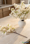 Artificial off-white cherry blossom arrangement in ceramic vase on marble countertop in modern warm kitchen interior