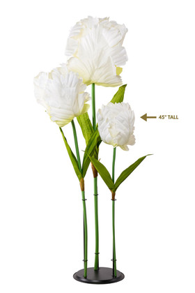 Oversized artificial white ivory silk tulip with multiple blooms and green leaves on tall stems, displayed on a black round stand for wedding or event decor.