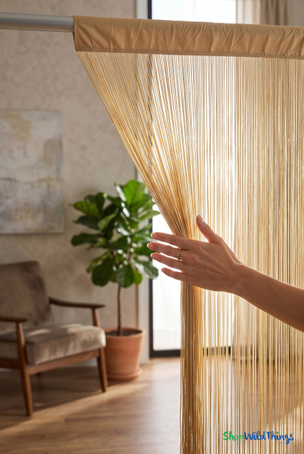 Woman’s hand parting the Light Gold Nassau Polyester & Cotton String Curtain Backdrop Over 400 Strands 35" Wide x 6' Long in a modern room — ShopWildThings.com