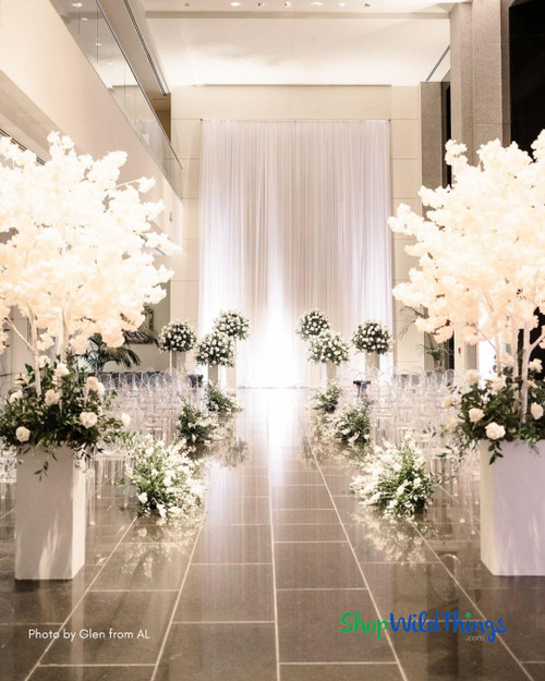 A touch of everlasting elegance – the 'Kenzie' tree by ShopWildThings.com gracefully adorning the aisle at a beautiful wedding. Bring timeless beauty to your events with our Artificial Flowering Trees! ?✨ 

We just restocked many of our most popular Artificial Flowering Trees, including the Kenzie in all 4 colors. Shop now before they sell out again!