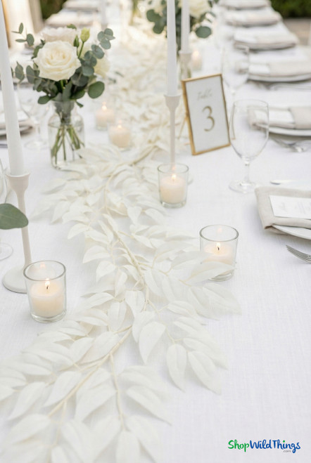 Close-up of white smilax leaf garland laid across a wedding reception table with glass votive candles and soft neutral place settings