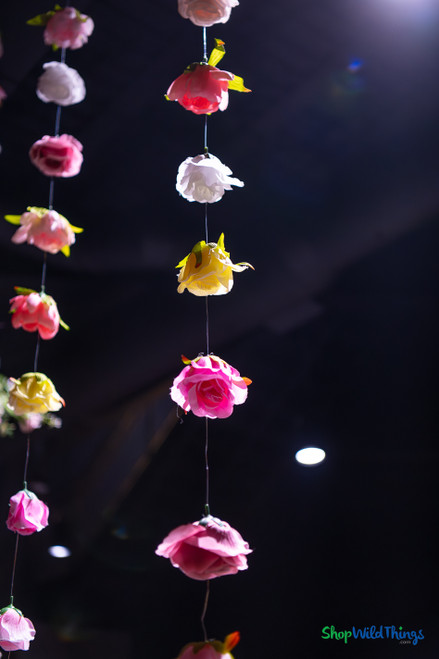 Colorful artificial flower garlands hanging from ceiling at event venue with floral greenery installation and dramatic lighting – ShopWildThings.com