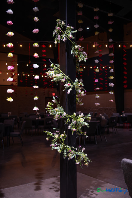 Colorful artificial flower garlands hanging from ceiling at event venue with floral greenery installation and dramatic lighting – ShopWildThings.com