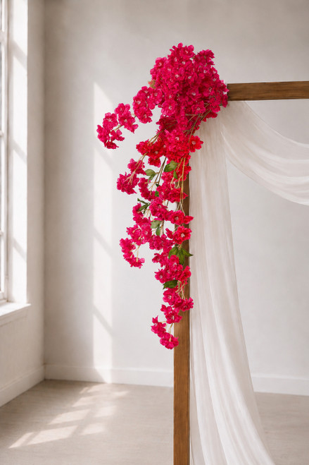 41" Fuchsia Pink Cascading "Spring Blossom" Spray – Extra-Full Silk Floral Waterfall from ShopWildThings.com attached to a simple wooden wedding arch in natural window light, with white fabric draping and fuchsia pink floral stems cascading downward.