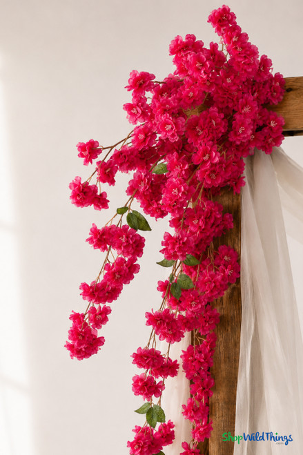 41" Fuchsia Pink Cascading "Spring Blossom" Spray – Extra-Full Silk Floral Waterfall from ShopWildThings.com styled on a wooden wedding arch with soft white draping, shown in a close-up detail view with bright fuchsia pink blooms and trailing floral sprays.
