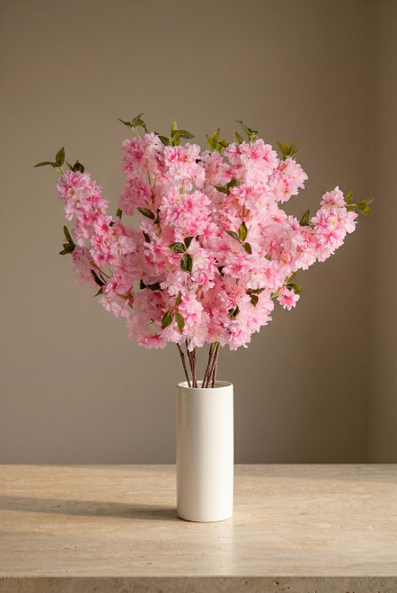 Light pink artificial cherry blossom branches arranged in white ceramic cylinder vase on stone tabletop, ShopWildThings.com event floral decor