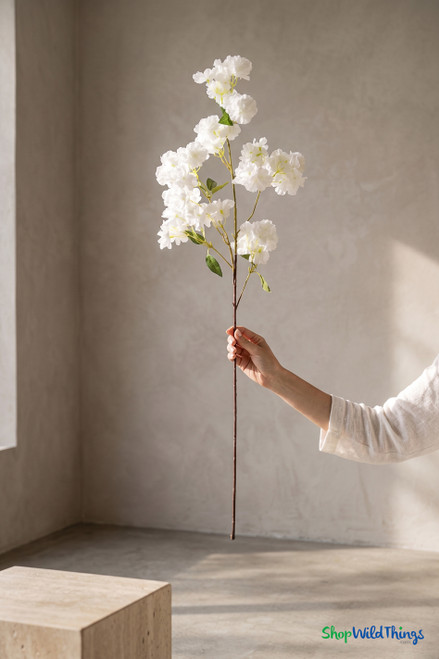 Hand holding a 40-inch artificial white cherry blossom branch for scale, showing full stem length, fluffy blooms, and realistic green leaves from ShopWildThings.com