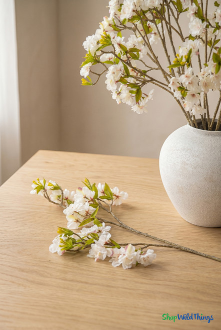 ShopWildThings artificial cherry blossom branches in white ceramic vase with single stem on wood table in warm minimal interior