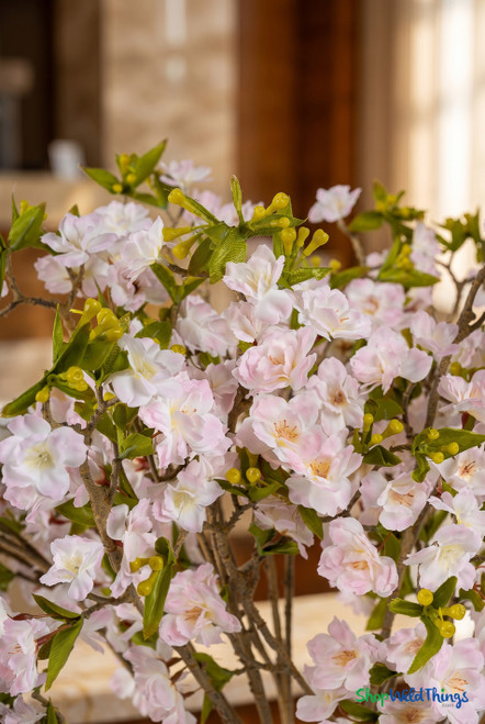 Close-up of artificial cherry blossom branches with soft pink and white blossoms green leaves and realistic buds in warm interior lighting