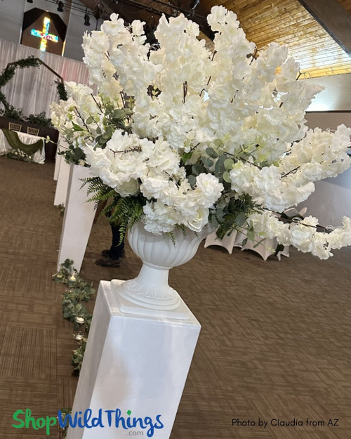Take a look at this elevated classic! Simple, elegant, and eye catching.  White Dogwood Branches styled in a White Grecian Urn Planter, on white pillar risers.  ShopWildThings.com makes it easy to make gorgeous wedding decor for your ceremony, aisle decor, and reception centerpieces.