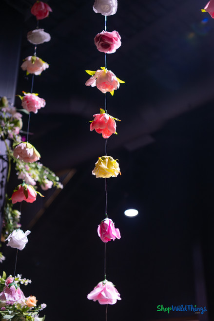 Colorful artificial flower garlands hanging from ceiling at event venue with floral greenery installation and dramatic lighting – ShopWildThings.com