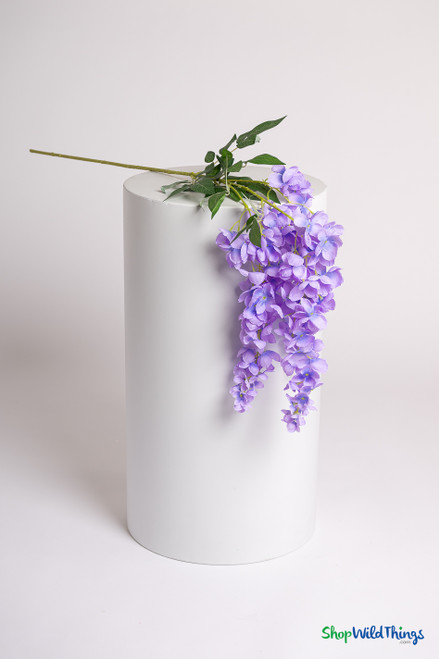 Lavender wisteria floral spray with cascading blooms displayed on a white pedestal, showing 45 inch artificial stem and green leaves from ShopWildThings.com