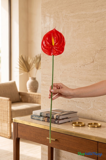 Real Feel Red Anthurium Tropical Stem, 27 inches tall, held by hand for scale in a warm resort-style interior, showing the long green stem and glossy red 6 inch bloom