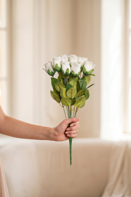 Young bridesmaid hand holding ivory silk rose bud bundle in a warm naturally lit indoor wedding venue for scale reference