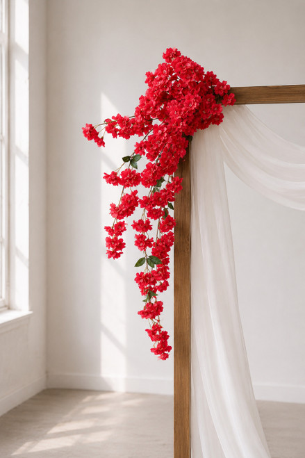 41" Red Cascading "Spring Blossom" Spray – Extra-Full Silk Floral Waterfall from ShopWildThings.com attached to a simple wooden wedding arch in natural window light, with white fabric draping and long red floral stems cascading downward.