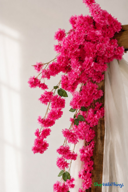41" Beauty Pink Cascading "Spring Blossom" Spray – Extra-Full Silk Floral Waterfall from ShopWildThings.com shown in a close-up wedding arch detail shot with soft pink silk blossoms, green leaves, brown stems, and draped white fabric.
