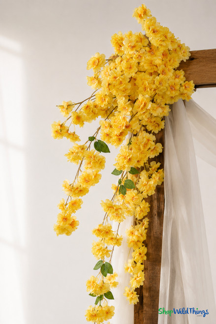 41" Yellow Cascading "Spring Blossom" Spray – Extra-Full Silk Floral Waterfall from ShopWildThings.com styled on a wooden wedding arch with soft white draping, shown in a close-up detail view with yellow blooms and trailing floral sprays.