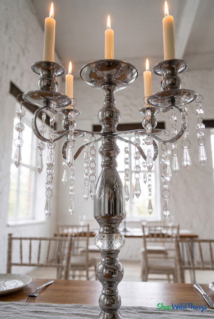 Close-up of the 18.75" Silver Metal Candelabra Centerpiece featuring polished metal arms, lit taper candles, and real glass crystal strands from ShopWildThings.com.