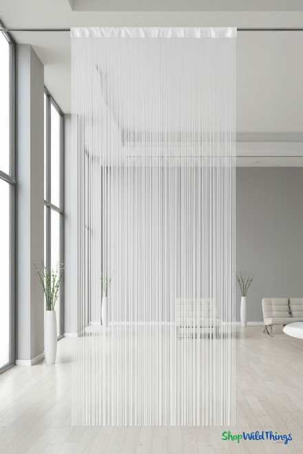 White 10-foot fire-rated string curtain hanging from a ceiling rod in a bright modern room with large windows, white walls, and minimalist décor. The silky off-white strands flow to the floor, creating an elegant divider ideal for weddings, events, or retail displays — ShopWildThings “Nassau” String Curtain backdrop.