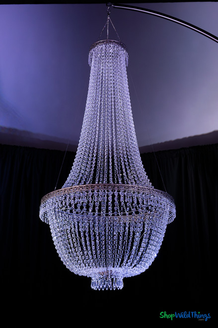Full-length vertical view of 5-foot Tillie Extra Large crystal-clear acrylic beaded empire chandelier suspended from curved rigging arm in event setting.