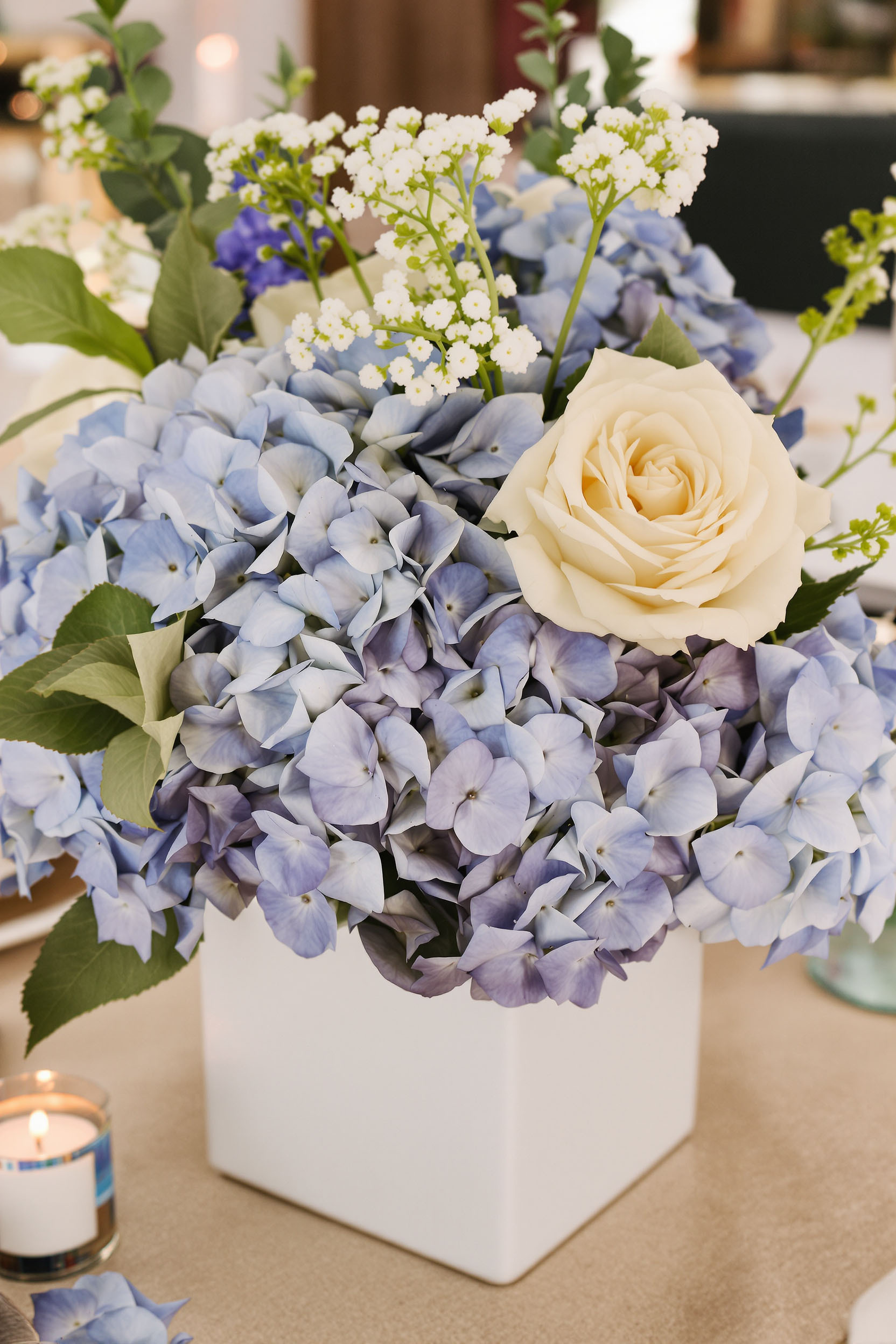 Seaside-Inspired Centerpiece with Blue Hydrangeas in a White Cube Vase Soft blue hydrangeas and cream roses evoke beachside elegance in this White Cube Vase arrangement, ideal for summer receptions.