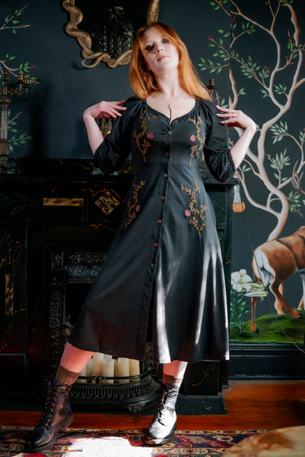 Model posing in black Persephone Summer dress, hands on shoulders, front view.