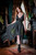 Woman posing in the Morrigan Apron Dress in grey with green embroidery in front of a mirror.