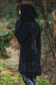Model posing in woods, showing adjustable lace up back of the Occultist Coat and large wide hood.
