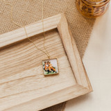 gold square photo pendant locket with gold chain, inside the jewelry sits a photo of children on a couch hugging