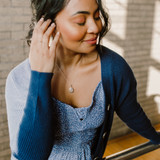 little silver oval keepsake locket modeled by a woman in blue sweater looking away from camera