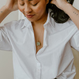 woman pulling hair back wearing white shirt and wearing The Emerald Calcite Pendant Necklace by The Locket Sisters