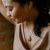 gold oval locket on woman in dress pulling hair back
