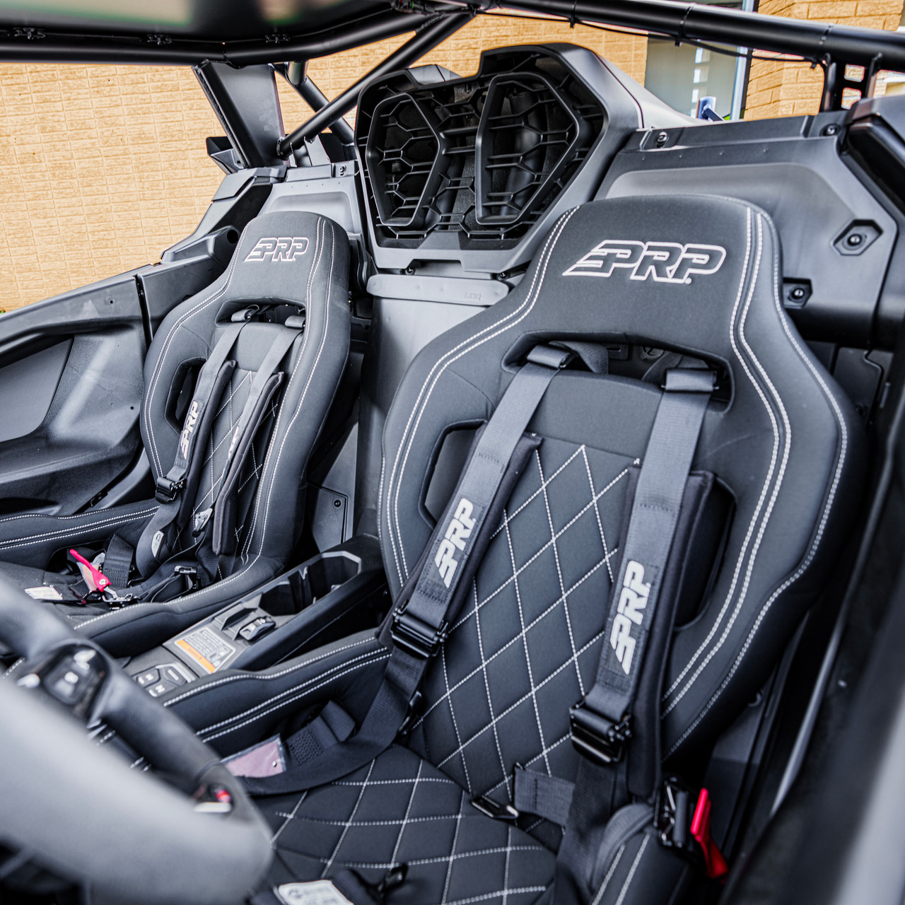 2026 Can-Am Maverick R, Green / Black, close-up of the cabin featuring two black PRP bucket seats with white stitching and racing harnesses.