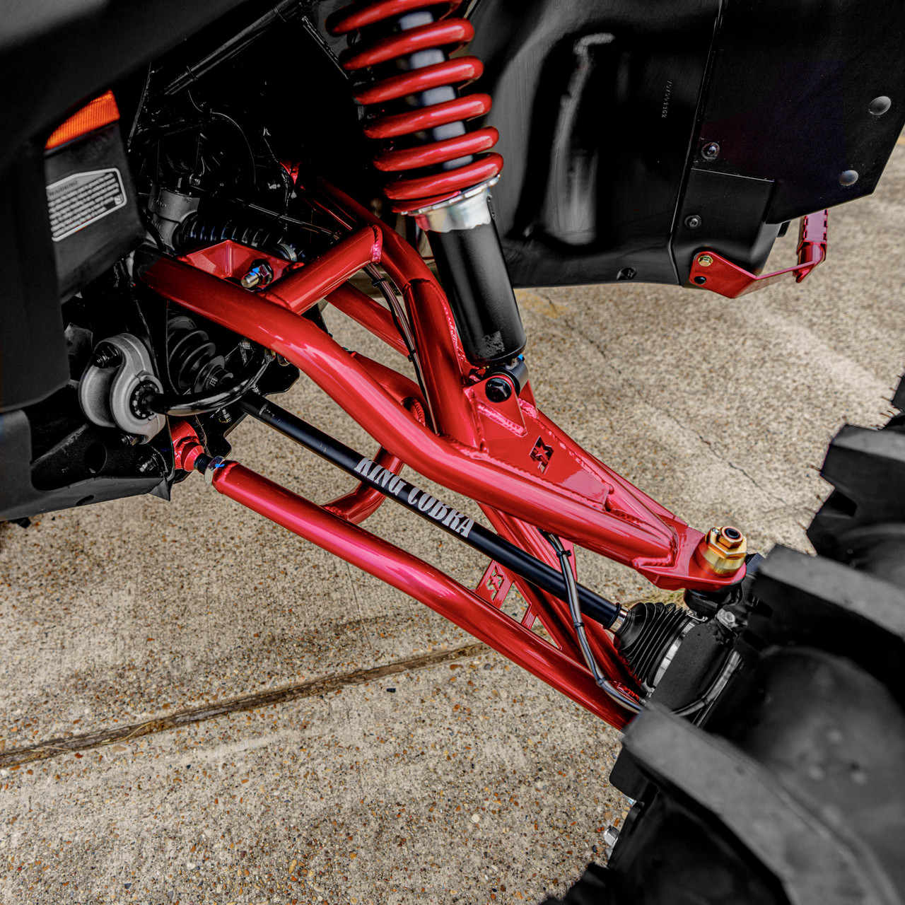 2026 Can-Am Defender HD11, close-up of the red front suspension, coil-over shock, and control arms beneath the black bodywork.