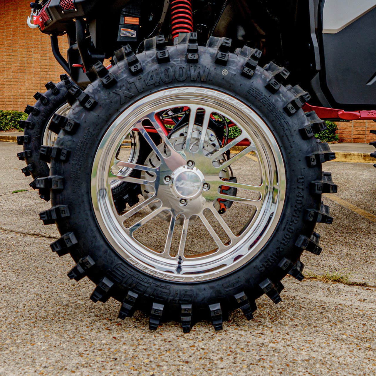 2026 Can-Am Defender HD11, close-up of a large knobby off-road tire and polished silver alloy wheel with red suspension springs and black bodywork